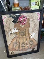 Framed shadowbox with 1920s beaded dress, white gloves, feather boa, beaded clutch purse, pink floral decoration, black feathered hat, and costume pearl jewelry arranged inside.
