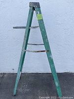 Side view of green fiberglass A-frame ladder with metal braces and paint marks