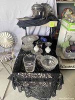 Several crystal bowls, goblets, ashtray, and silver plated trays arranged on a black lace cloth on tables and an adjustable stand with wheels.