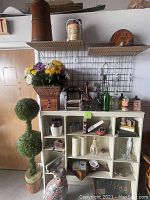 View of hutch with artificial plants, ceramic cat, trinket boxes, candles, and glass bottles with hanging wire rack and shelves above