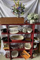 Full view of the red wooden shelf showing all items arranged on shelves including silk flowers, kitchen items, glass jars, ceramic dishes, and wooden box