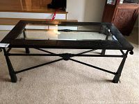 Glass and metal coffee table showing side view highlighting metal legs with cross braces and decorative embossed perimeter frame.