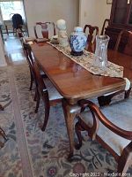 Full view of the large wood dining table with chairs and table decorations, showing one leaf in place and polished surface.