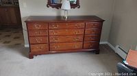 Front view of the mahogany dresser with twelve drawers and brass handles on a beige carpet.