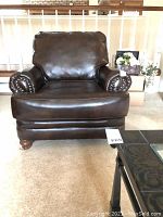 Front-side angle of dark brown leather club chair with wooden bun feet, showing armrests and seat cushion.