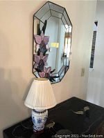 Stained glass mirror mounted on wall above a black table with a blue and white floral ceramic table lamp with pleated shade.