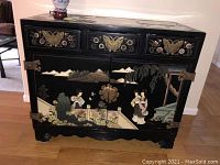 Front view of oriental lacquer cabinet with three drawers and two doors displaying painted scenes and floral motifs