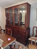 Front view of two-piece cabinet showing four glass-paneled doors on hutch top and carved drawers and doors on base