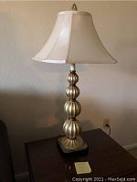 Metal table lamp with segmented rounded column design, hexagonal cream fabric shade, and finial topper. Lamp is approx. 32 inches tall.