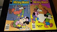 Two front covers of the Walt Disney Mickey Mouse comics, one with Goofy asleep on piping and the other titled 'The Inca Idol Mystery'
