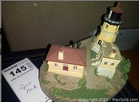 Front angled view of the Split Rock Lighthouse resin model showing the lighthouse tower, adjacent buildings, and textured rocky base.