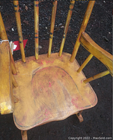 Close up of wooden seat with visible distress and antiqued paint finish with yellow and red tones.