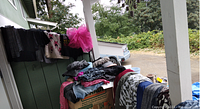 Pile of assorted women's clothing items draped over boxes and railing outdoors, showing multiple colors and textures including knitwear and denim.