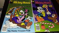 Two vintage Mickey Mouse comic books with colorful cartoon covers, one titled 'The Timber Treasure Trail'