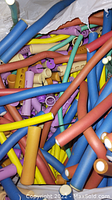 Photo showing many colorful hollow plastic hair rollers and curlers in a white bag.