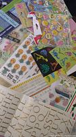 Photo shows various scrapbook sticker sheets spread out including emoji, dinosaurs, alphabet letters, and floral borders.