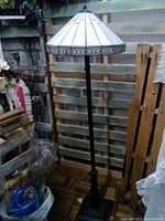 Full view of the Tiffany style floor lamp approximately 5 feet tall with stained glass shade and black metal stand.