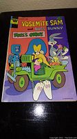 Front cover of the Yosemite Sam and Bugs Bunny comic book featuring Bugs Bunny and a robot in a green jeep-like vehicle.