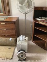 Photo showing the Lasko white oscillating pedestal stand fan, the smaller white Duracraft table fan, and the white Honeywell air purifier with manual booklet placed on the floor and furniture.