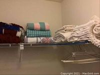 Shelf with various folded blankets and throws, including multicolored knitted afghan, pastel striped throw, houndstooth pattern, and patchwork quilt visible