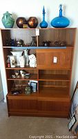 Front view of the wood bookcase displaying open shelves, upper and lower sliding doors, and various decorative items on shelves (not included in sale).