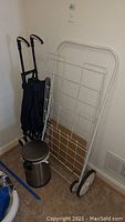 Lot items together in corner: wastebasket with foot pedal, metal folding shopping cart, and folding canvas cart.