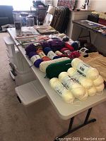 Table with an assortment of yarn skeins, knitting needles, crochet hooks, and crafting magazines