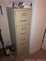 Full view of beige metal filing cabinet with four drawers and metal handles. Box of Pendaflex file folders seen on top.