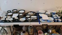 Wide angle photo showing Lifetime plastic folding table with various dishes and pottery underneath and on top.