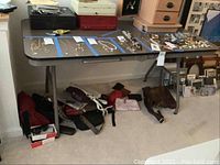 Full view of folding event style table with some jewelry and other items placed on top, bags and other items underneath. Table legs in folded position supporting the table.