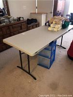 Full view of the folding table with a plastic surface and black metal legs showing some crafting supplies on the table.