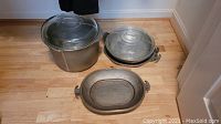 Wide angle photo showing all three vintage aluminum Guardian Ware pots and pans arranged on a wooden floor.