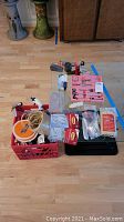 Overview of all lot items arranged on floor, showing crate with tools, nylon cord, hanging strips, tool kit, hammer, sisal rope, tape measure, and small hardware.