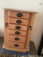 Closed view of wooden jewelry box showing 5 front drawers with dark metal pulls and side latch handles.