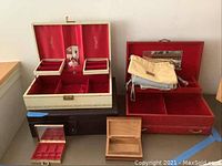 Photo showing four jewelry boxes: a large white faux leather jewelry box with gold detailing, a large red jewelry box with red velvet lining and ballerina figurine, a small wooden box, and a small red earring box with compartments.