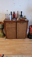 Front view of wood server cabinet with woven cane panel doors and various items on top.