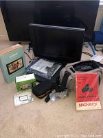 Photo showing Toshiba 19 inch TV with various accompanying items including Portal box, Garmin GPS, Panasonic video recorder carrying bag, and Magnavox camera manual.