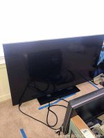 Samsung 50 inch flat screen TV with black bezel and stand, laid on carpet with connected power cable.