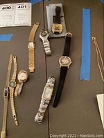 Photo showing 7 vintage watches arranged on a table with various dial shapes and band styles.