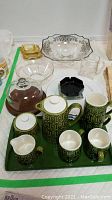 Green ceramic coffee serving set with tray and various pieces including coffee pot, mugs, creamer and sugar bowl shown with glass ashtrays and bowls