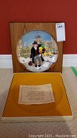 Photo of the Royal Doulton collector's plate "The Balloon Man" mounted on wood mount, leaning against wall with the box below