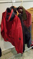 Three men's jackets hanging on a rail, showing red, navy, and burgundy colors.