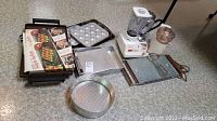 Full overview of kitchen items including blender, food chopper, baking trays, cooling rack and waffle pans.