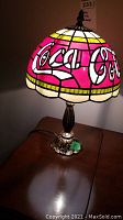 Front angled view showing the Coca Cola logo on the stained glass style shade and metal base.