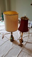 Pair of brass lamps on a white cloth surface, showing height difference and distinct lampshades.