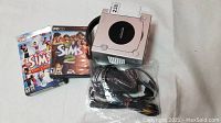 Nintendo GameCube console top view, closed, with Sims and Sims 2 PC game cases and cables in plastic bag