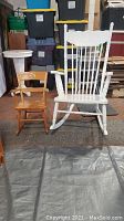 Adult white painted wooden rocking chair with a press back design and child's natural wood rocker side by side.