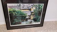 Framed color print of garden scene with a door, matted and framed in black.