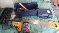Wide view of the lot displaying toolbox, saw, corded drill, drill bits, and other hand tools on tarp.
