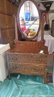 Front and angled view of vintage wooden vanity showing oval mirror with carved floral scrolls and drawer details
